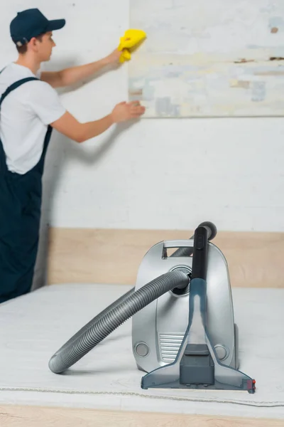 Selective focus of vacuum near young man in uniform cleaning painting — Stock Photo