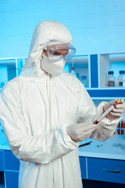 Scientist in hazmat suit and goggles holding test tube with coronavirus lettering — Stock Photo