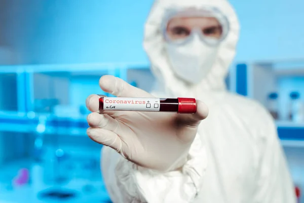 Selective focus of scientist in hazmat suit, medical mask and goggles holding sample with coronavirus lettering — Stock Photo