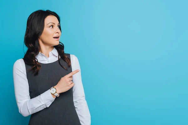 Shocked businesswoman looking away and pointing with finger isolated on blue — Stock Photo