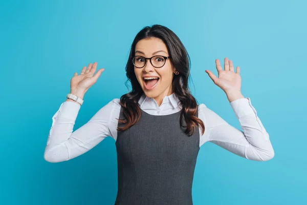 Happy businesswoman showing wow gesture while looking at camera on blue background — Stock Photo