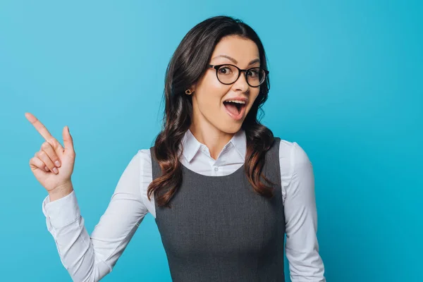 Geschockte Geschäftsfrau mit Brille zeigt mit Finger auf blau — Stockfoto