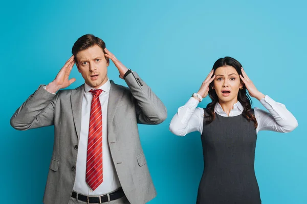 Two exhausted businesspeople touching heads while suffering from migraine on blue background — Stock Photo