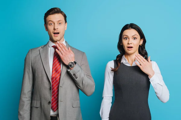 Two shocked businesspeople looking at camera while standing with open mouths on blue background — Stock Photo