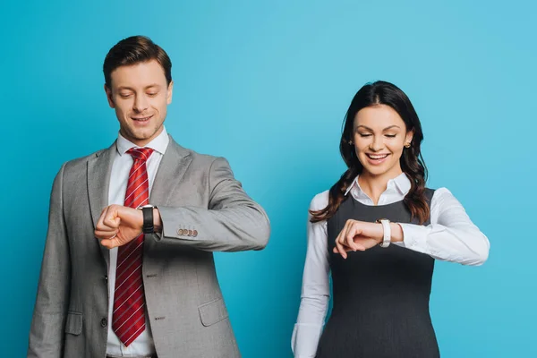 Uomo d'affari e donna d'affari sorridente guardando orologi da polso su sfondo blu — Foto stock