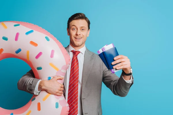 Cheerful businessman with swim ring showing passports and air tickets on blue background — Stock Photo