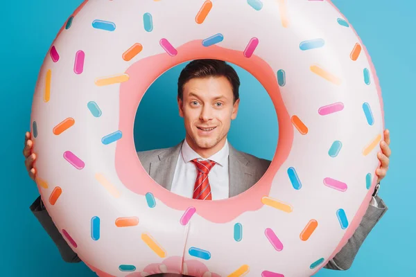 Smiling businessman with swim ring looking at camera on blue background — Stock Photo