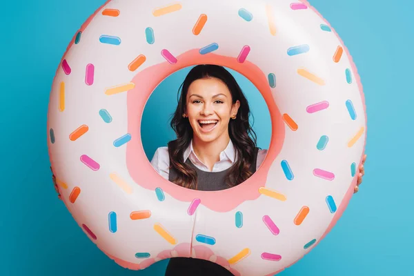 Cheerful businesswoman with swim ring smiling at camera on blue background — Stock Photo