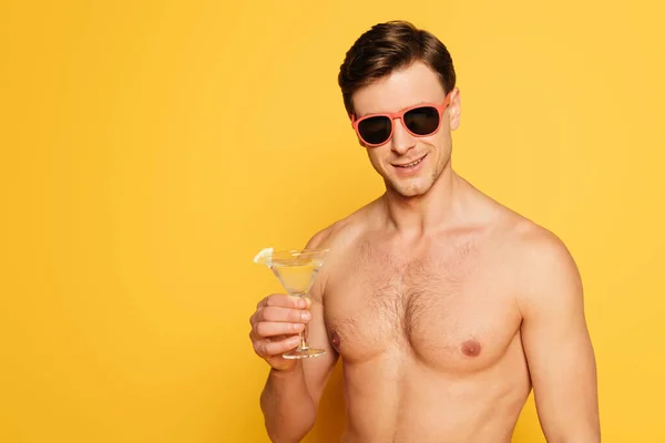 Shirtless man in sunglasses holding glass of cocktail on yellow background — Stock Photo