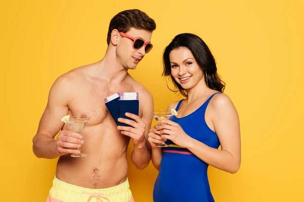 Heureux couple avec des verres de cocktail, passeports et billets d'avion sur fond jaune — Photo de stock