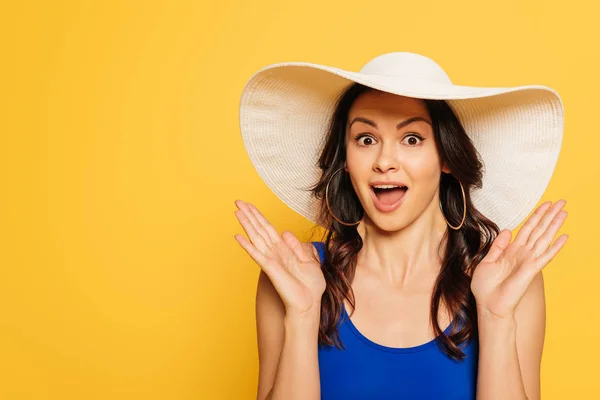 Attractive, surprised woman in sun hat showing wow gesture isolated on yellow — Stock Photo