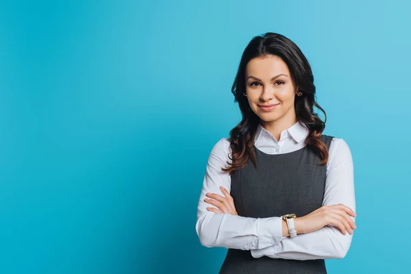 Smiling businesswoman standing with crossed arms and looking at camera on blue — Stock Photo