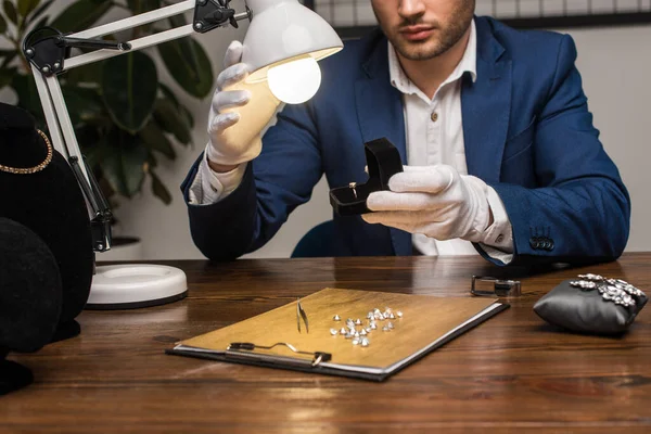 Vista recortada del anillo de fijación del tasador de joyas con gemas en caja cerca de la lámpara en la mesa - foto de stock