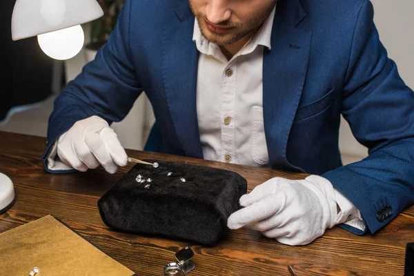 Ausgeschnittene Ansicht eines Schmuckgutachters, der Edelstein in einer Zange in der Nähe einer Lampe auf einem Tisch in der Werkstatt hält — Stockfoto