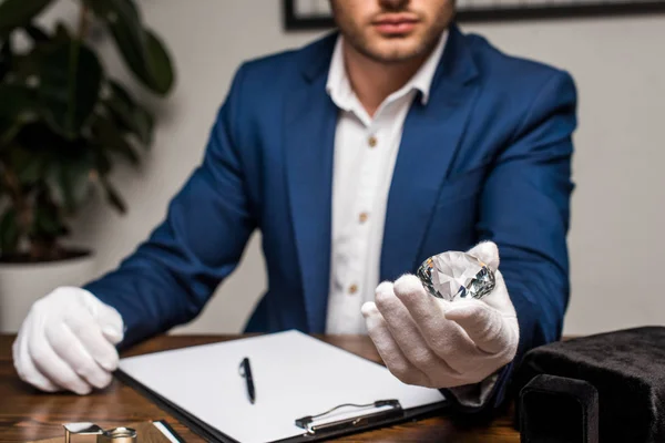 Selective focus of jewelry appraiser holding gemstone near clipboard on table — Stock Photo