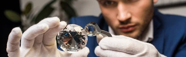 Selective focus of jewelry appraiser examining gemstone with magnifying glass, panoramic shot — Stock Photo