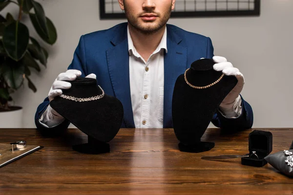 Обрізаний вигляд ювелірного оцінювача, що тримає намисто, стоїть з намистами біля ювелірних виробів на столі в майстерні — стокове фото