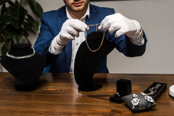 Ausgeschnittene Ansicht des Schmuckgutachters in Handschuhen mit Halskette in der Nähe von Schmuck auf dem Tisch in der Werkstatt — Stockfoto