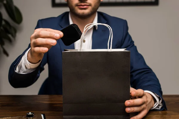 Vue recadrée de l'évaluateur de bijoux tenant la boîte près du sac en papier sur la table — Photo de stock