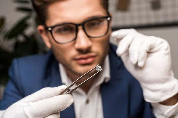 Selective focus of jewelry appraiser holding gemstone in tweezers while working in workshop — Stock Photo