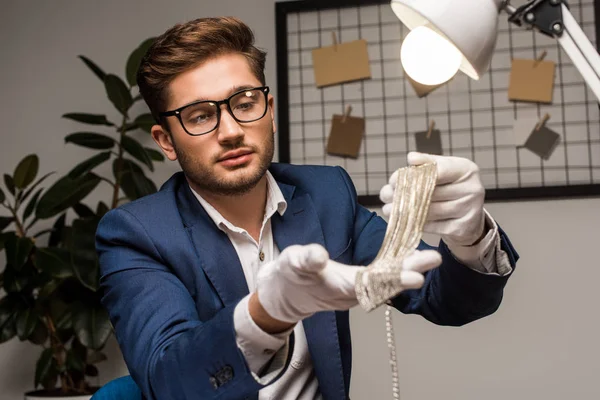 Selective focus of jewelry appraiser holding necklace near lamp in workshop — Stock Photo