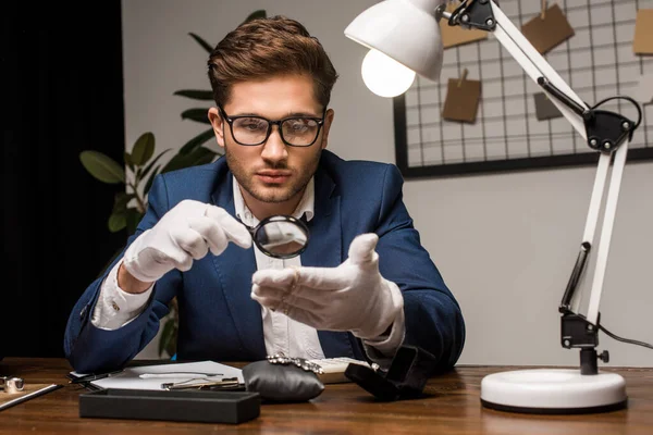 Schmuckgutachter untersucht Armband mit Lupe in der Nähe von Schmuck auf Tisch — Stockfoto