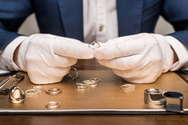 Vue recadrée de l'évaluateur de bijoux tenant bague de bijoux près de bord et loupe sur table isolée sur gris — Photo de stock