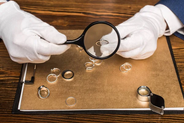 Ausgeschnittene Ansicht des Schmuckgutachters mit Schmuckring und Lupe in der Nähe der Tafel auf dem Tisch — Stockfoto