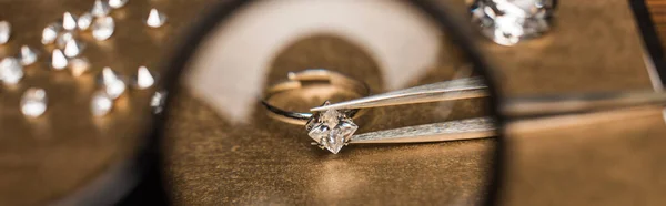 Selective focus of magnifying glass, jewelry ring with gemstone in tweezers on board, panoramic shot — Stock Photo