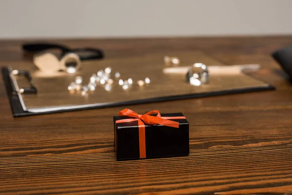 Selective focus of gift box near gemstones on board on table isolated on grey — Stock Photo