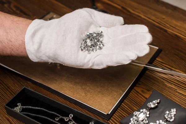 Cropped view of jewelry appraiser holding gemstones near jewelry and board on table isolated on grey — Stock Photo