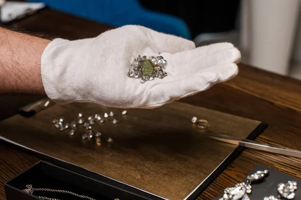 Cropped view of jewelry appraiser holding ring and gemstones near jewelry and board on table — Stock Photo