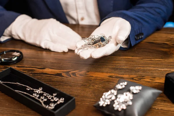 Vista cortada de jóias avaliador segurando jóias perto de lupa na mesa sobre fundo preto — Fotografia de Stock