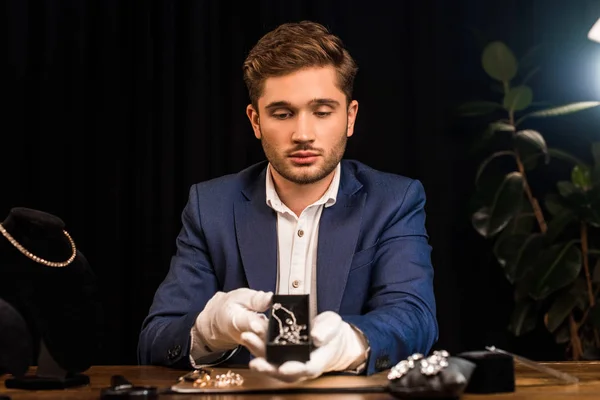 Jolie boîte à bijoux évaluateur tenant avec collier près de bijoux sur la table dans l'atelier — Photo de stock