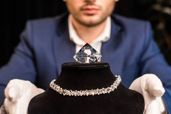 Cropped view of jewelry appraiser holding necklace stand with necklace and gemstone on black background — Stock Photo