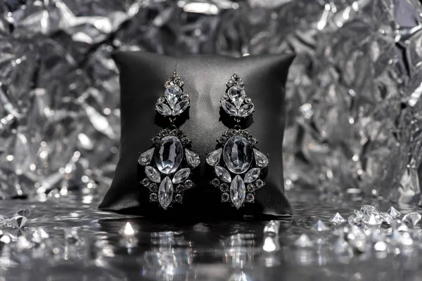 Ganhos de jóias no travesseiro de jóias perto de pedras preciosas no fundo de prata texturizado — Fotografia de Stock