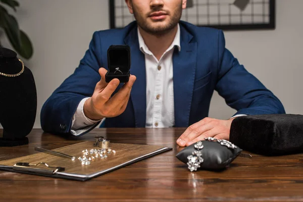 Cropped view of jewelry appraiser holding box with jewelry ring near jewelry and tools on table in workshop — Stock Photo