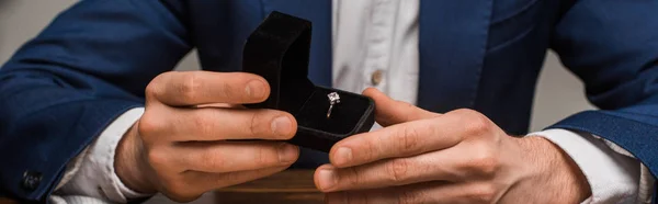 Cropped view of jewelry appraiser holding box with jewelry ring at table isolated on grey, panoramic shot — Stock Photo