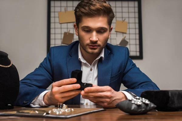 Selektiver Fokus des Schmuckgutachters hält Schatulle mit Schmuckring in der Nähe von Schmuck in der Werkstatt auf dem Tisch — Stockfoto