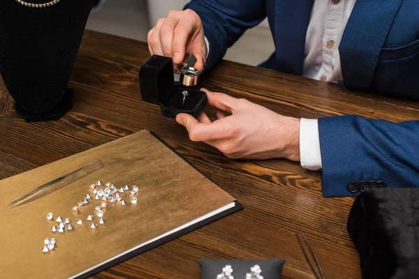 Vista cortada do avaliador de jóias examinando anel de jóias com lupa perto de pedras preciosas na mesa de madeira — Fotografia de Stock