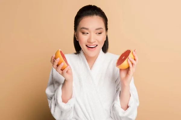 Happy beautiful asian woman in bathrobe with grapefruit halves on beige background — Stock Photo