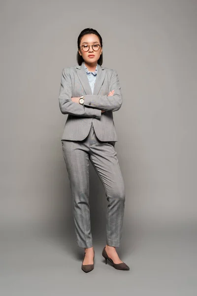 Jeune femme d'affaires en lunettes avec les bras croisés sur fond gris — Photo de stock