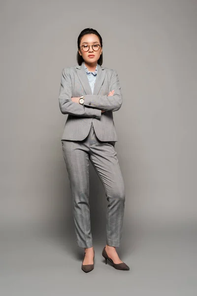 Young businesswoman in eyeglasses with crossed arms on grey background — Stock Photo