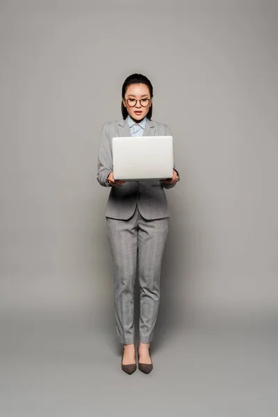 Молодая деловая женщина в очках с ноутбуком на сером фоне — стоковое фото