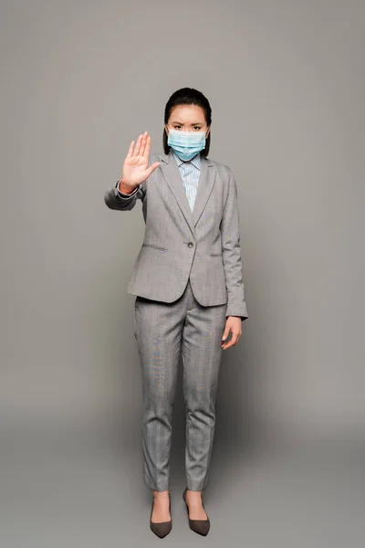 Молодая предпринимательница в медицинской маске показывает стоп-жест на сером фоне — стоковое фото