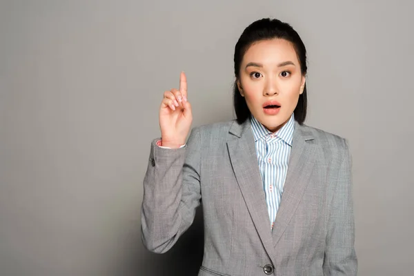 Aufgeregte junge Geschäftsfrau im Anzug zeigt Ideengeste auf grauem Hintergrund — Stockfoto