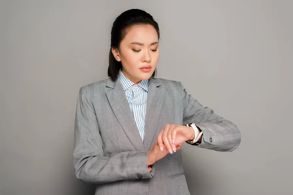 Junge Geschäftsfrau im Anzug schaut auf Armbanduhr auf grauem Hintergrund — Stockfoto