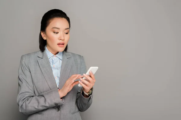 Young businesswoman in suit using smartphone on grey background — Stock Photo