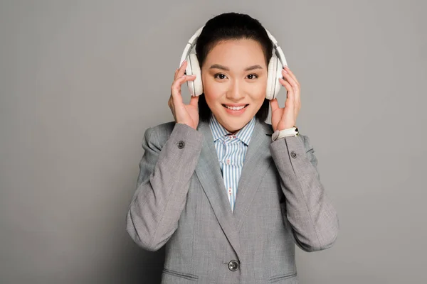 Sorridente jovem empresária em fones de ouvido em fundo cinza — Fotografia de Stock