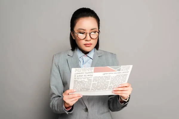 Jovem empresária em óculos lendo jornal em fundo cinza — Fotografia de Stock